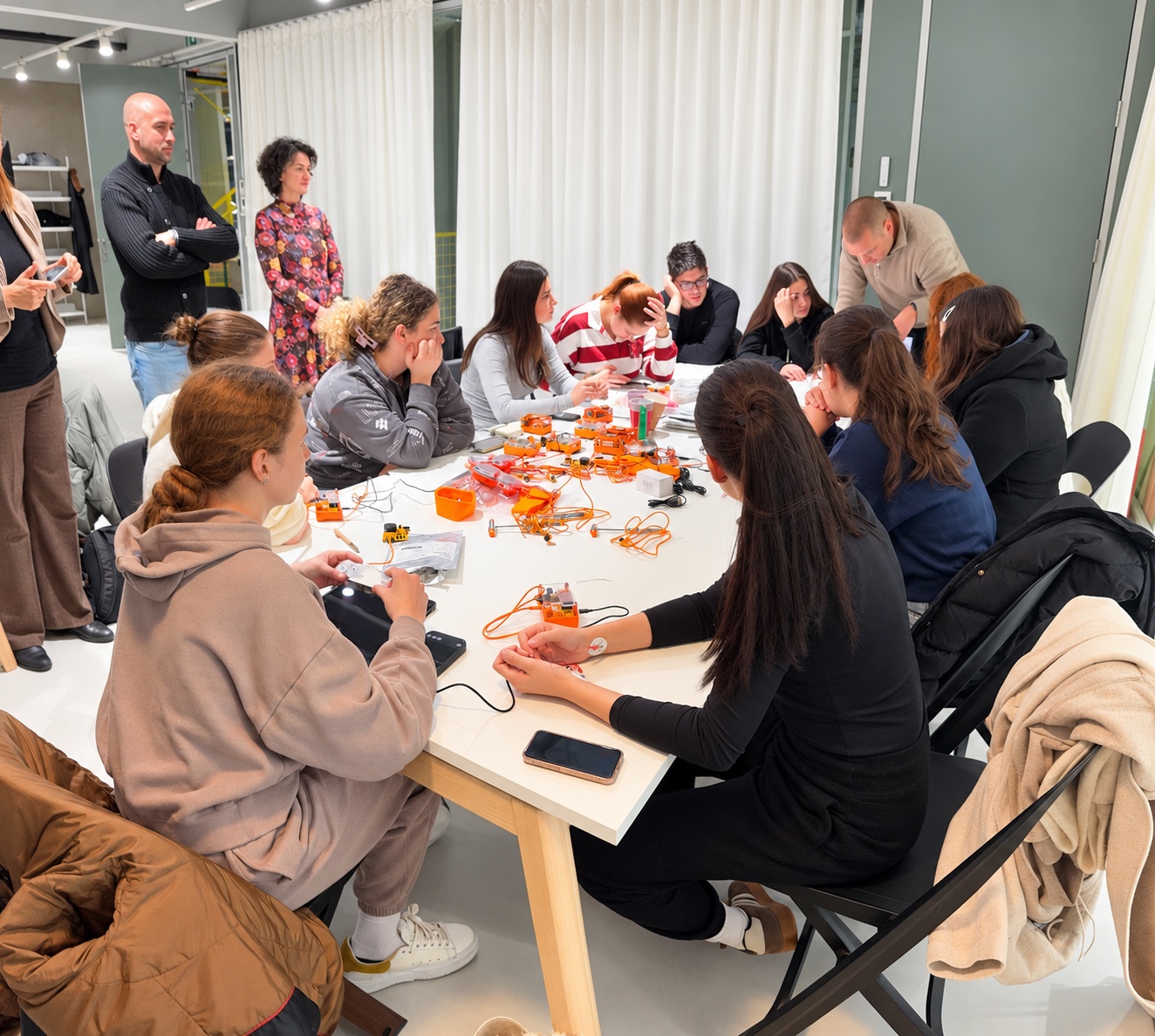 Students and community members gather around a table of orange Backyard Brains recording kits during a workshop at ARC Ložionica, while educators look on